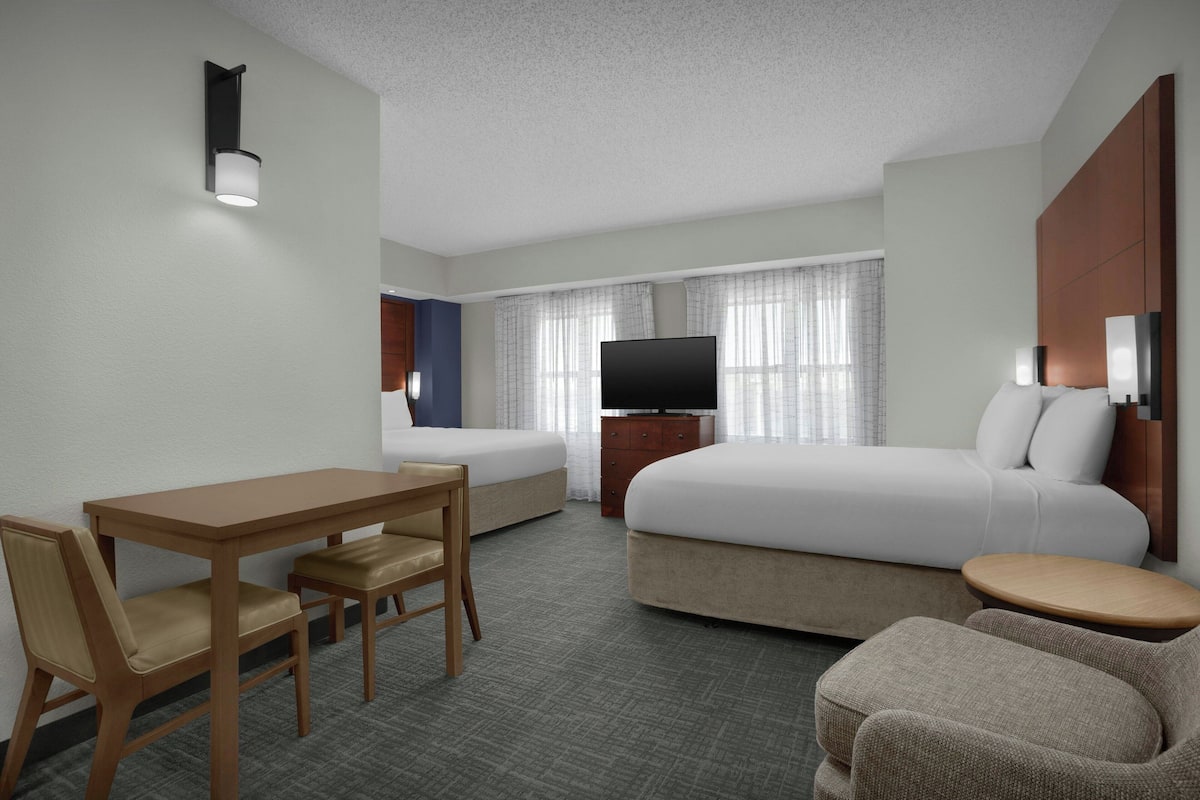 A hotel room with a bed, a TV, a desk with chairs, and a small round table.