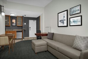 A modern living room with a sofa, ottoman, dining table, chairs, kitchen area, and framed pictures on the wall. - Residence Inn Portland Downtown/Waterfront (Portland)