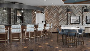 Un espace bar avec des tabourets, un comptoir et un mur orné d’un motif en chevrons.