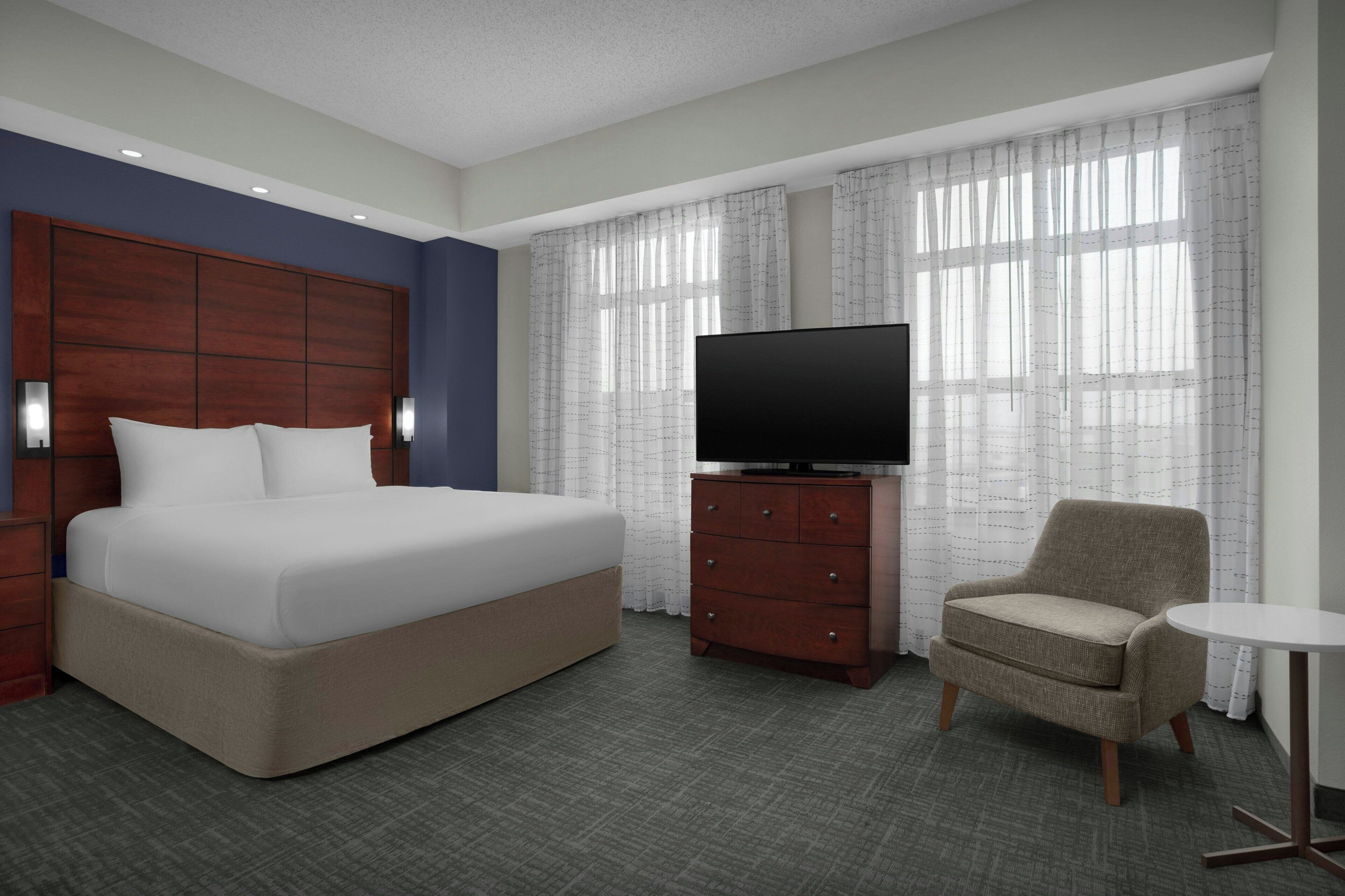 A hotel room with a large bed, a television on a wooden dresser, a chair, and a small round table.