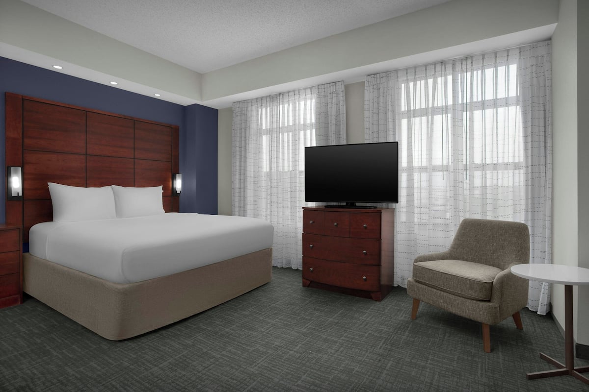 A hotel room with a large bed, a television on a wooden dresser, a chair, and a small round table.