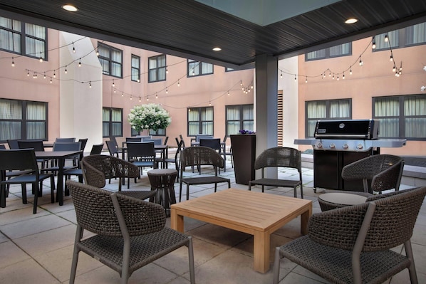 An outdoor patio area with wicker furniture, string lights, and a barbecue grill. - Residence Inn Portland Downtown/Waterfront (Portland)