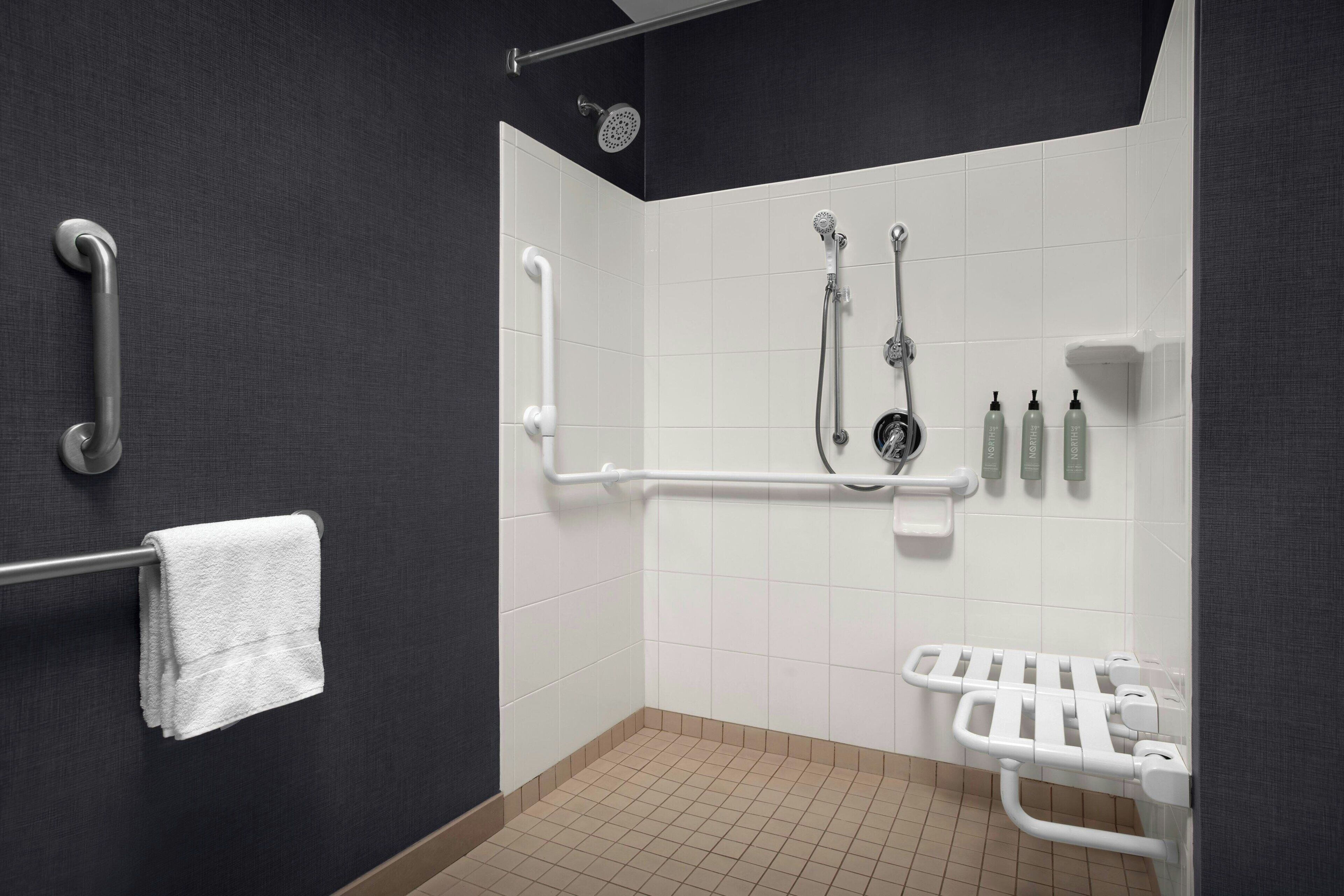 A bathroom with a shower, grab bars, a towel rack, and a hand dryer.