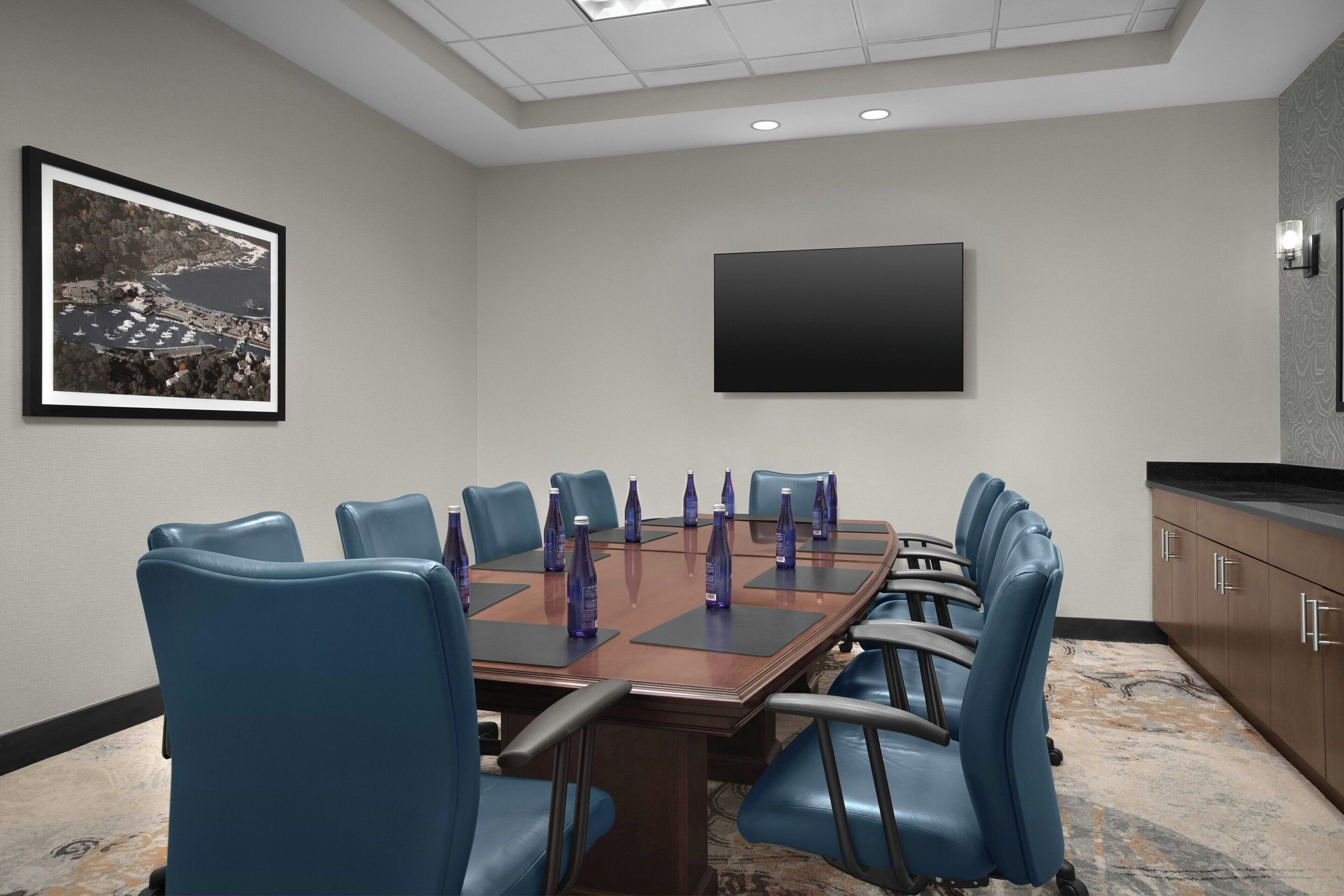 Una sala conferenze con un grande tavolo, sedie blu, una TV a schermo piatto e un quadro appeso al muro.
