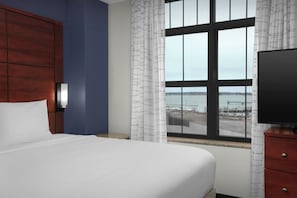 A hotel room with a bed, a TV, a nightstand, a window with a view of the water, and a wooden headboard. - Residence Inn Portland Downtown/Waterfront (Portland)
