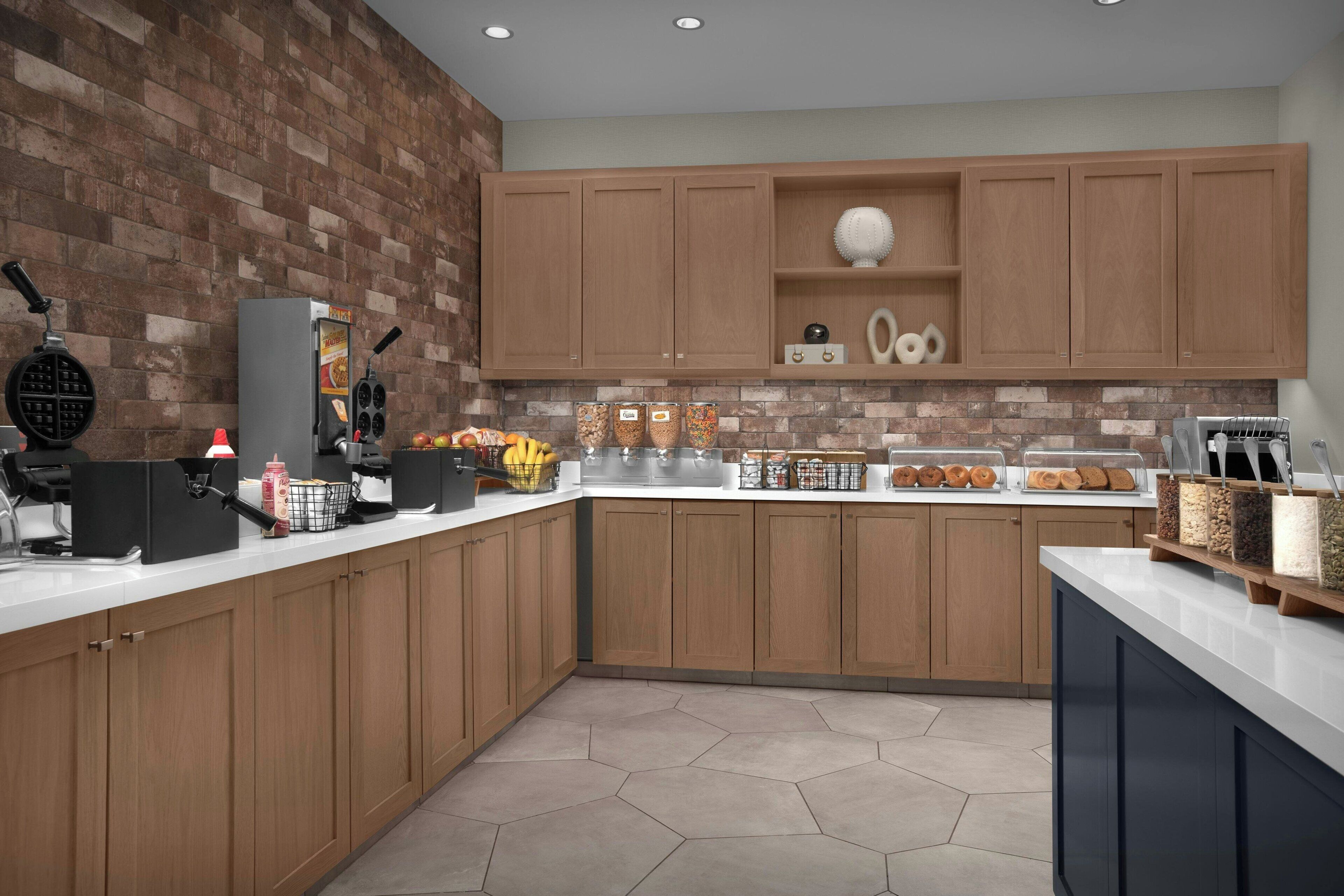 A modern kitchen with wooden cabinets, a brick wall, and a countertop with various food items and kitchen appliances.