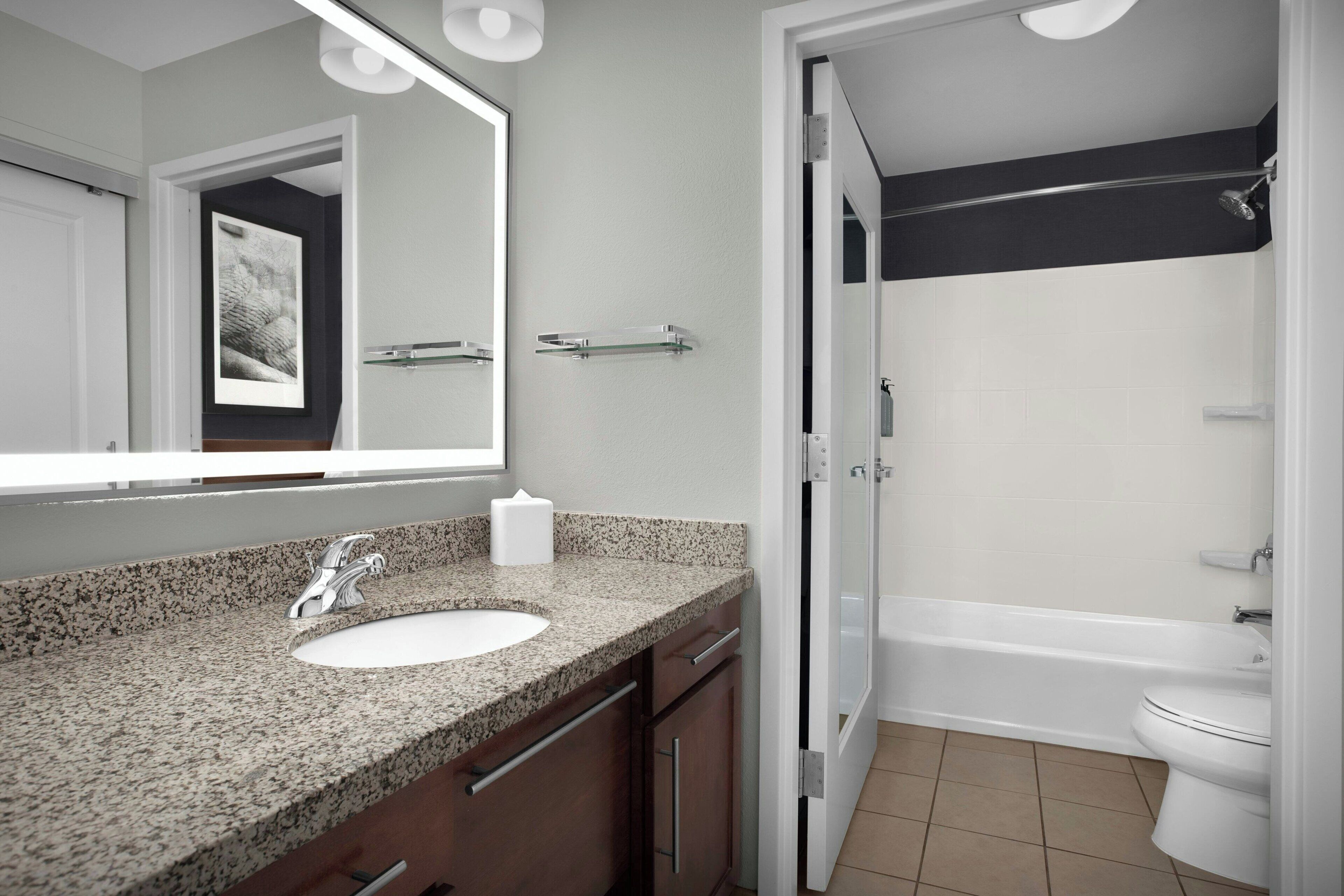A bathroom with a granite countertop sink, a mirror, a shower, and a toilet.