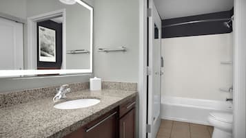 A bathroom with a granite countertop sink, a mirror, a shower, and a toilet.