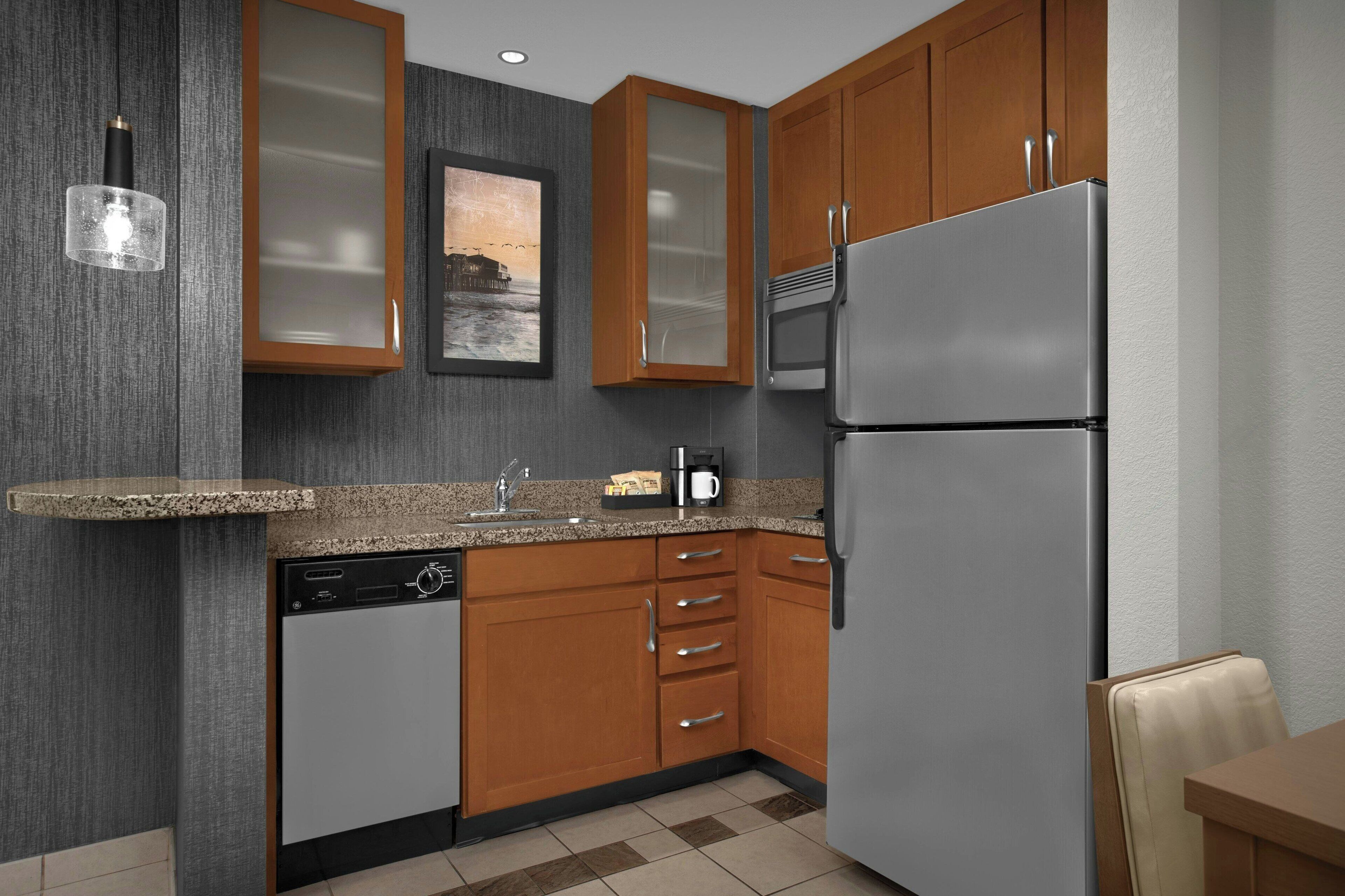A modern kitchen with wooden cabinets, a stainless steel refrigerator, a dishwasher, and a granite countertop.