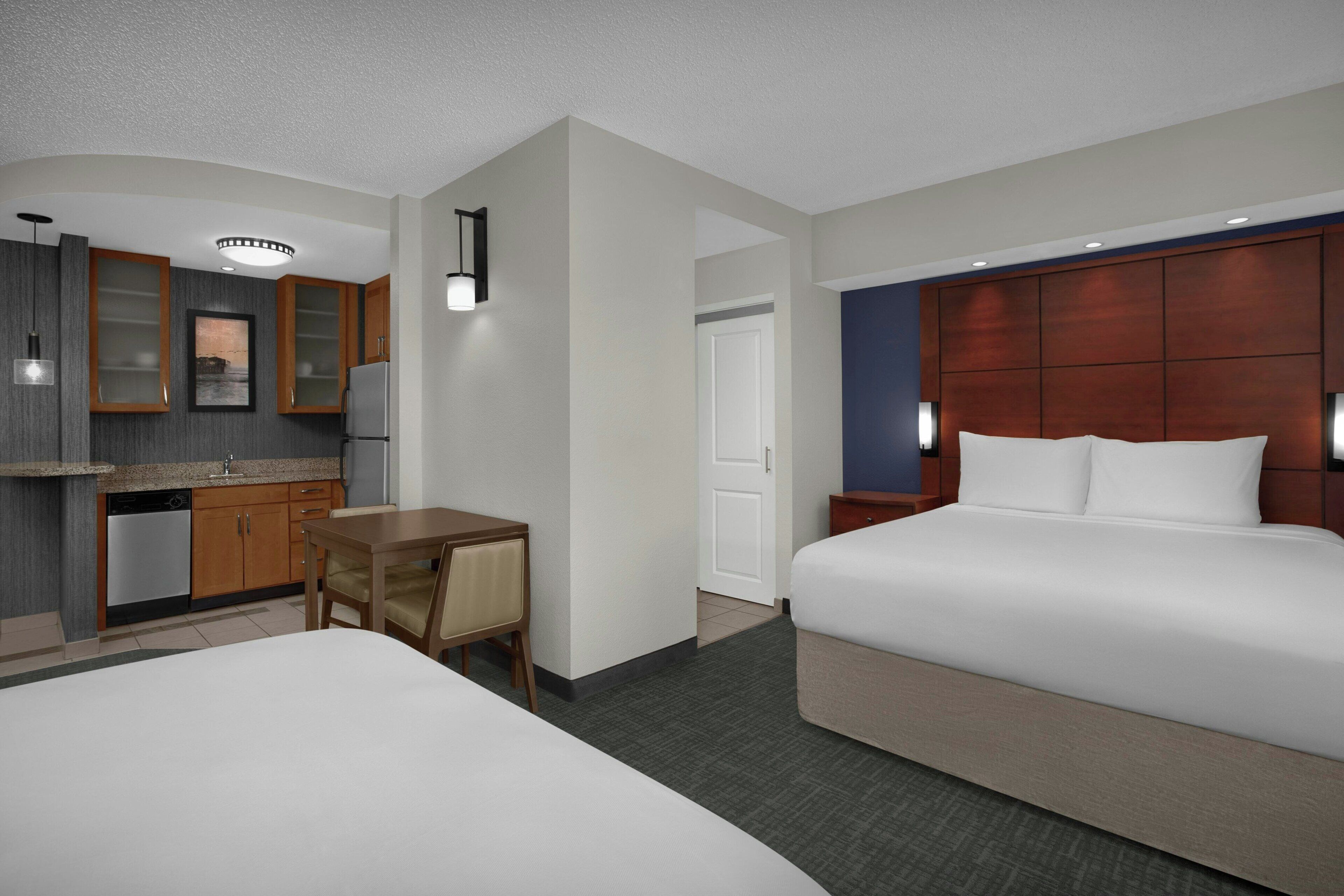 A hotel room with a bed, a desk, a kitchenette, and a bathroom.