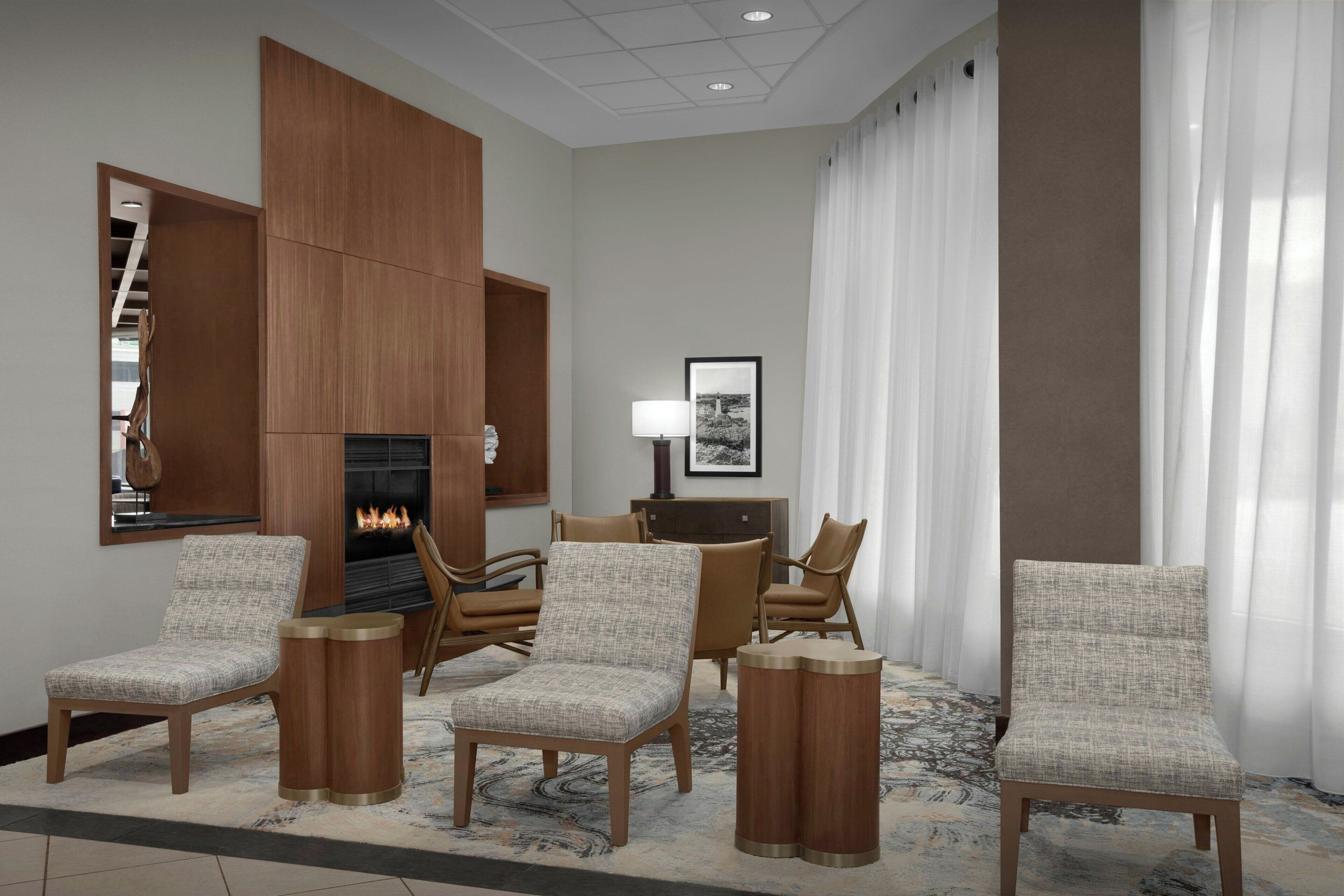 A hotel lobby with a fireplace, four armchairs, a sideboard, and a framed picture on the wall.