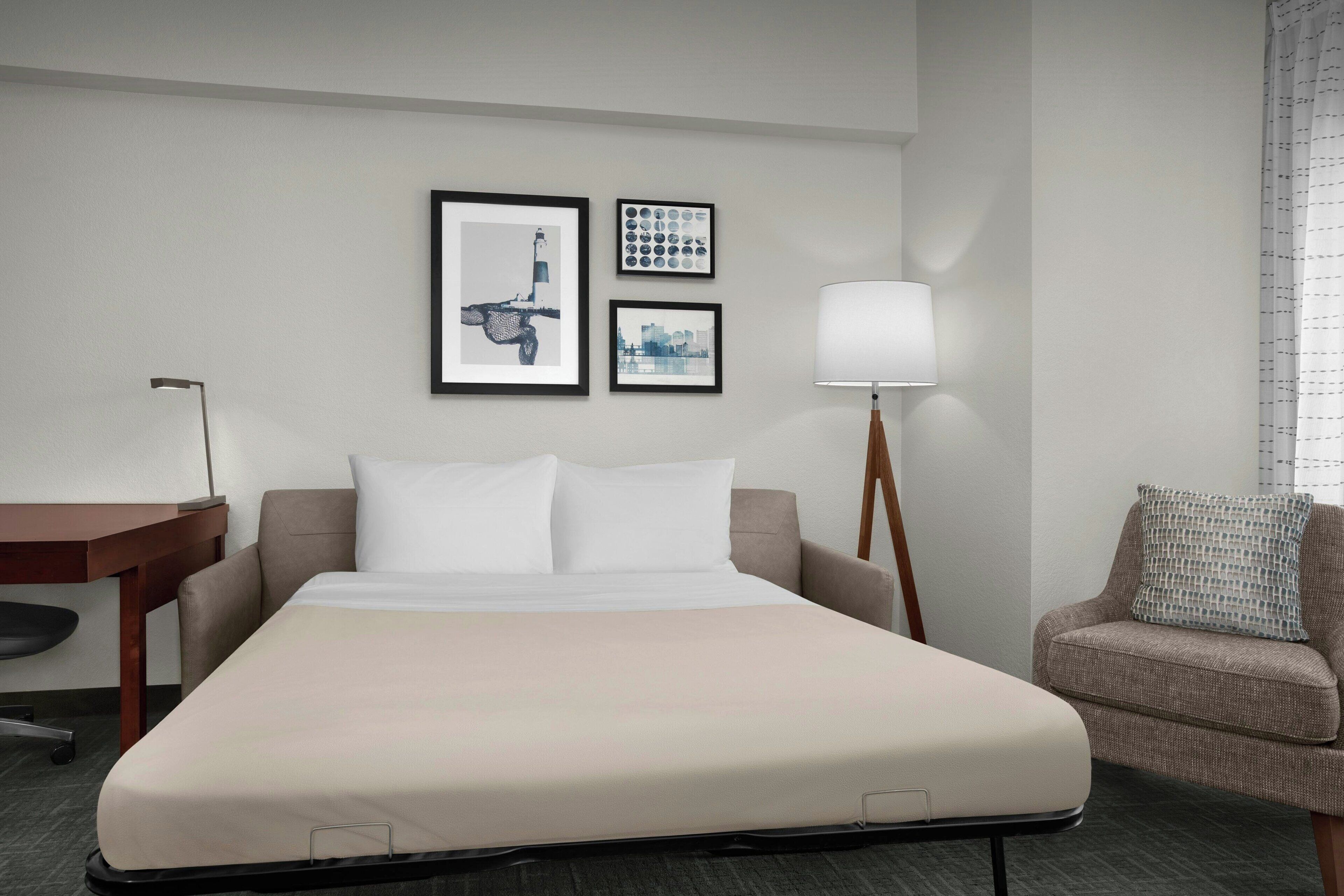 A hotel room with a bed, a desk, a chair, and a lamp.