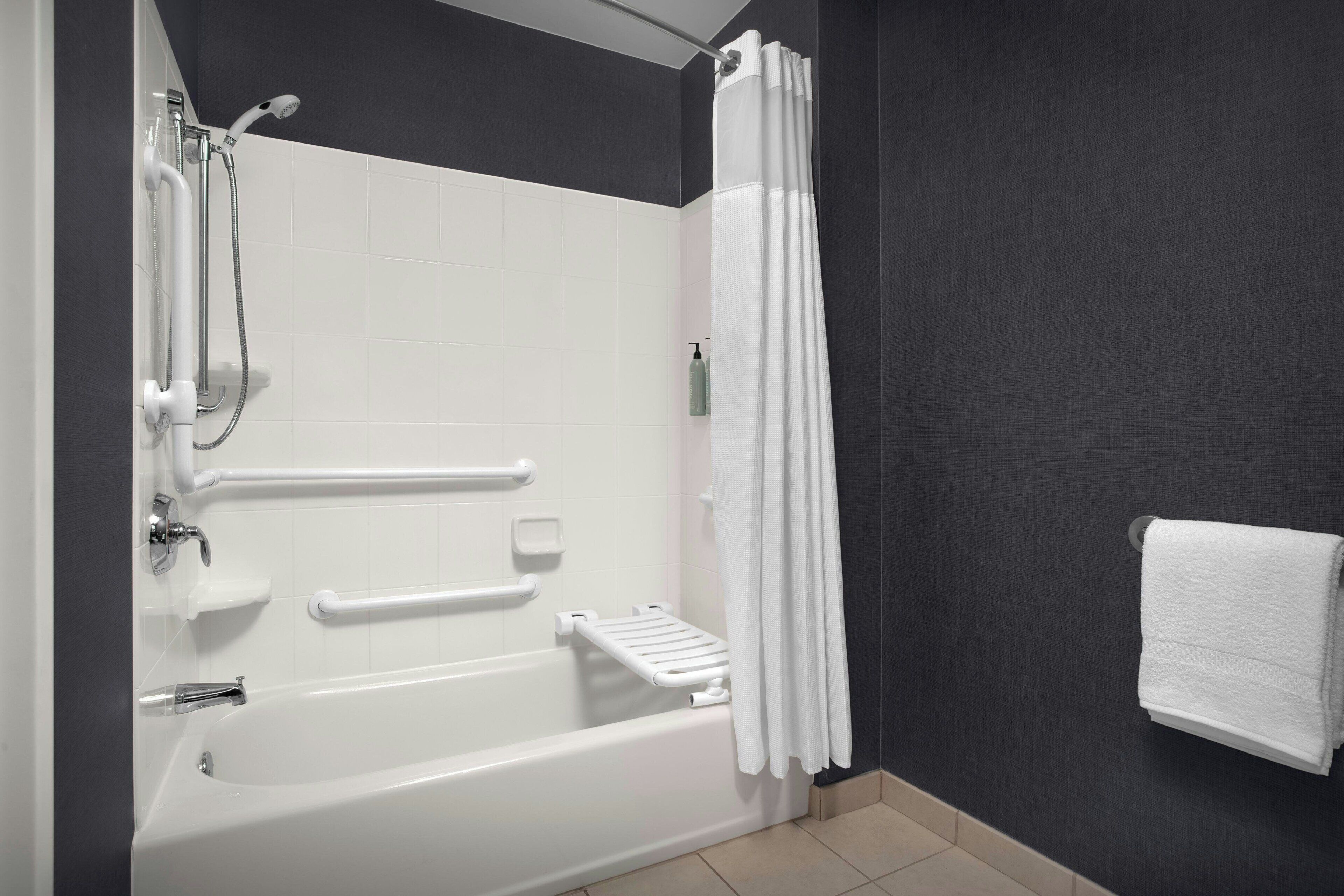 A modern bathroom with a bathtub, shower, handrails, and a towel rack.