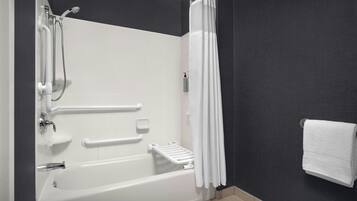 A modern bathroom with a bathtub, shower, handrails, and a towel rack.
