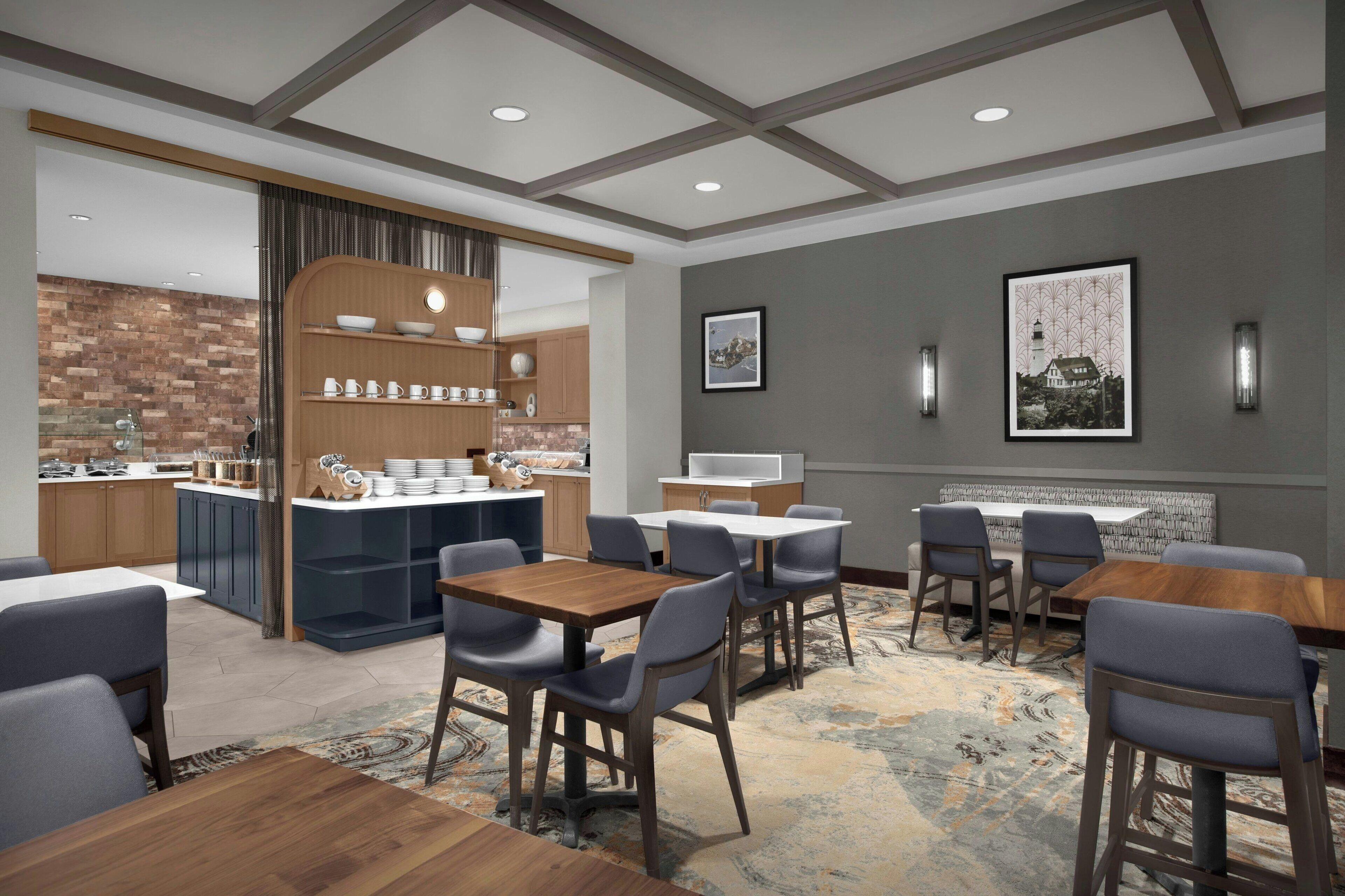 Un hall d’hôtel moderne doté d’un bar, de coins salon et d’une cheminée.