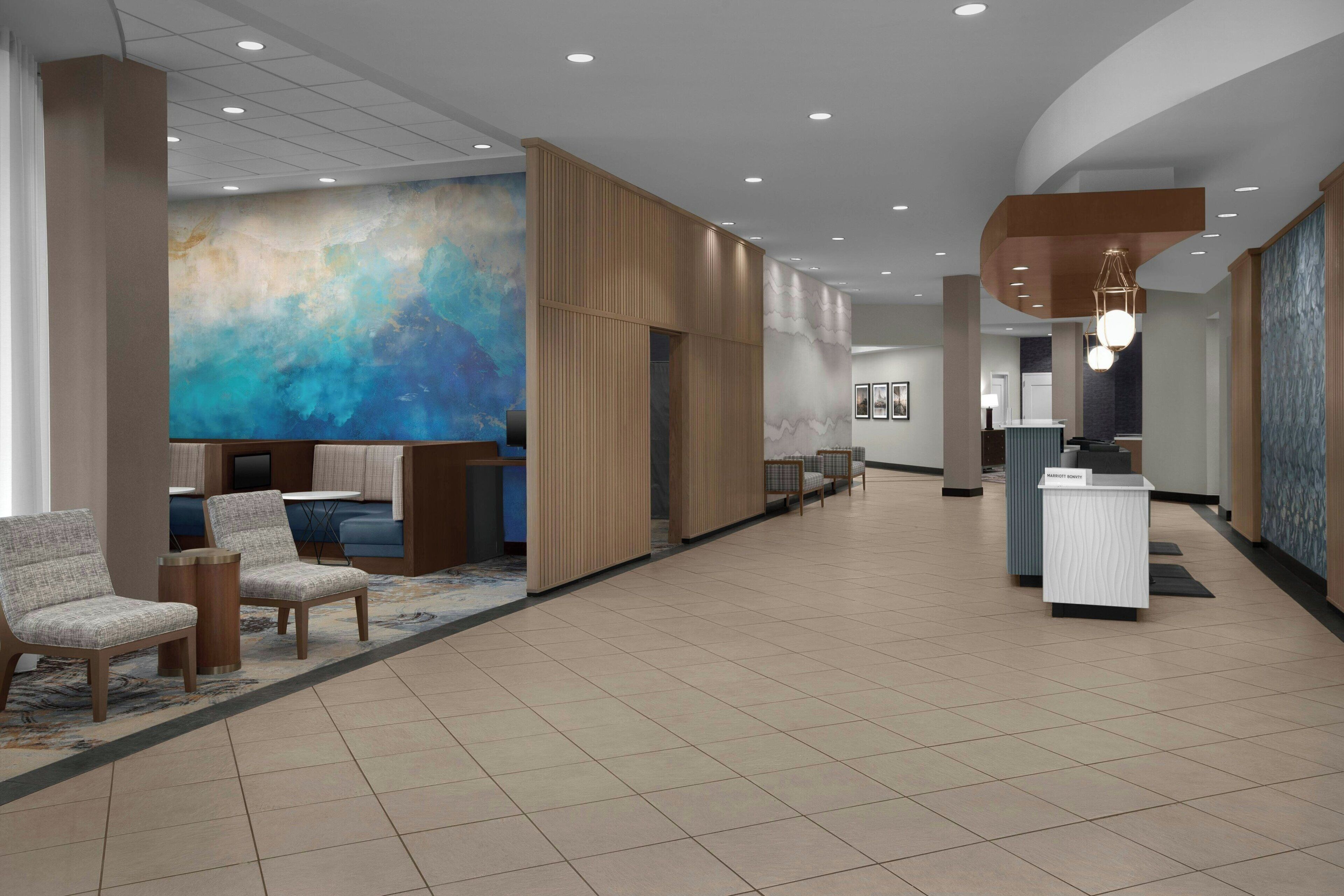 A spacious lobby with seating areas, a reception desk, and a large abstract mural on the wall.