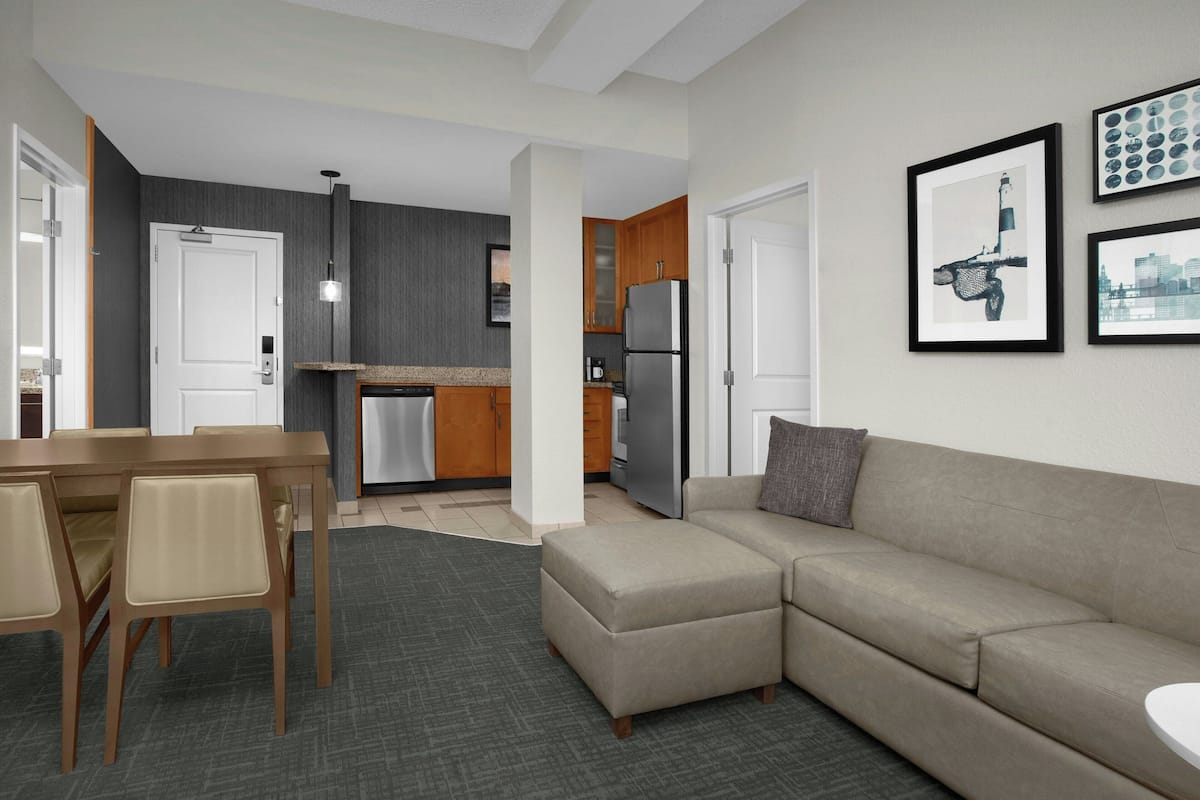 A modern kitchen with a refrigerator, a dining area with a table and chairs, and a living area with a sofa.