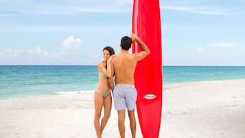 A couple standing on a beach with a red surfboard.