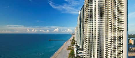 A high-rise hotel with a curved facade, located adjacent to a beach with a clear view of the ocean.