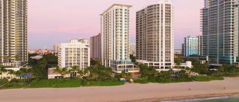 A beachfront hotel with multiple high-rise buildings, a sandy beach, and a clear view of the ocean.