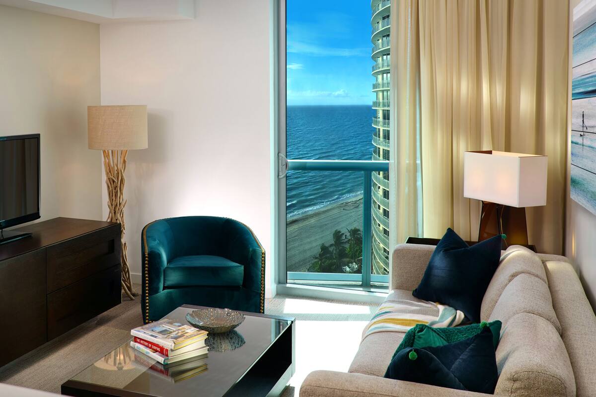 A modern hotel room with a large window offering a view of the ocean and a cruise ship.