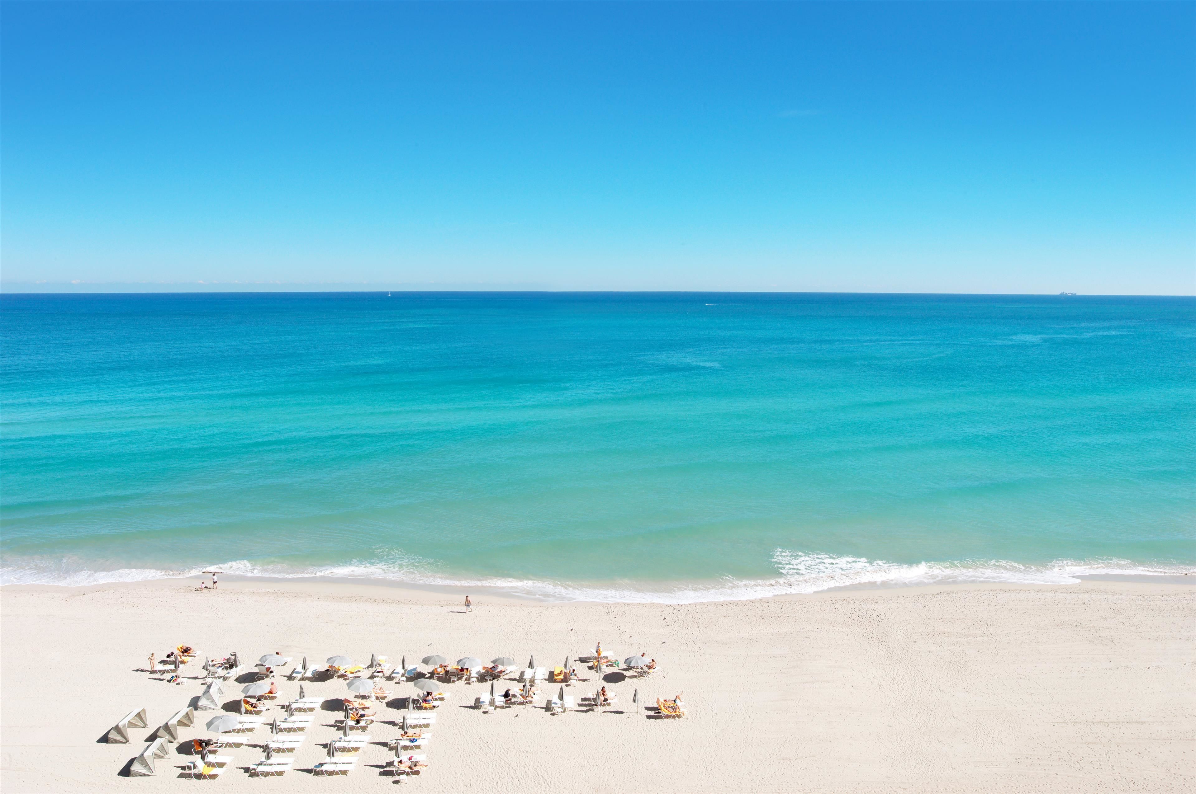 A beach with clear turquoise water and a sandy shore. There are sun loungers and umbrellas arranged on the beach.