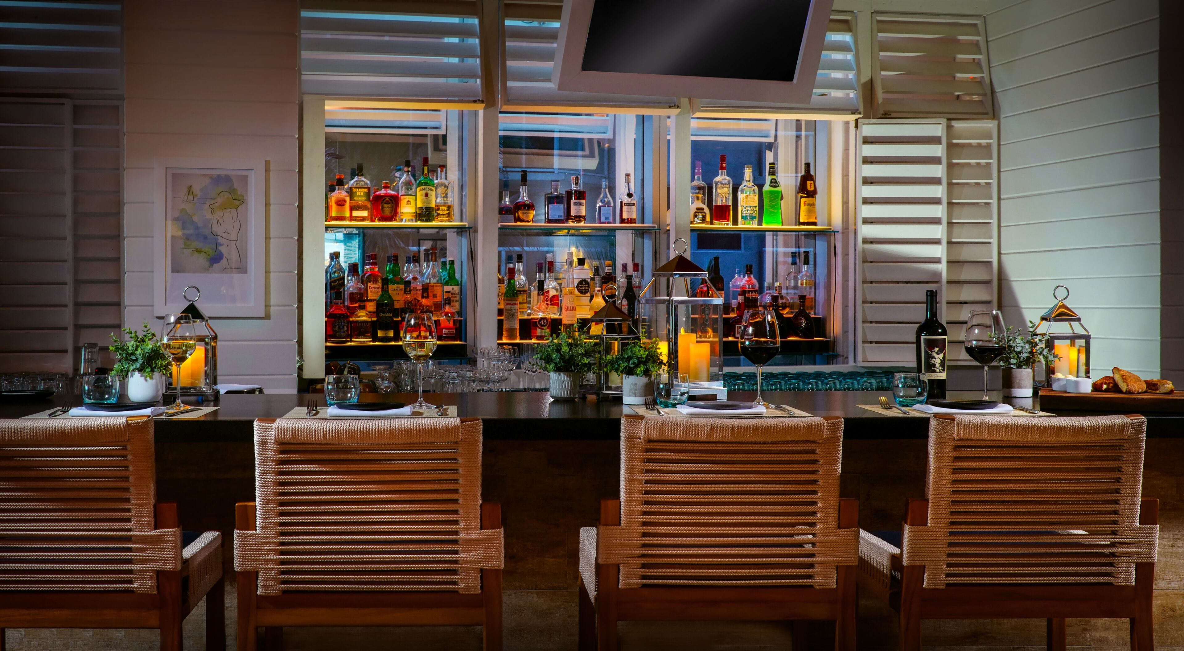A bar area with multiple shelves of liquor bottles, wicker chairs, and a well-lit interior.