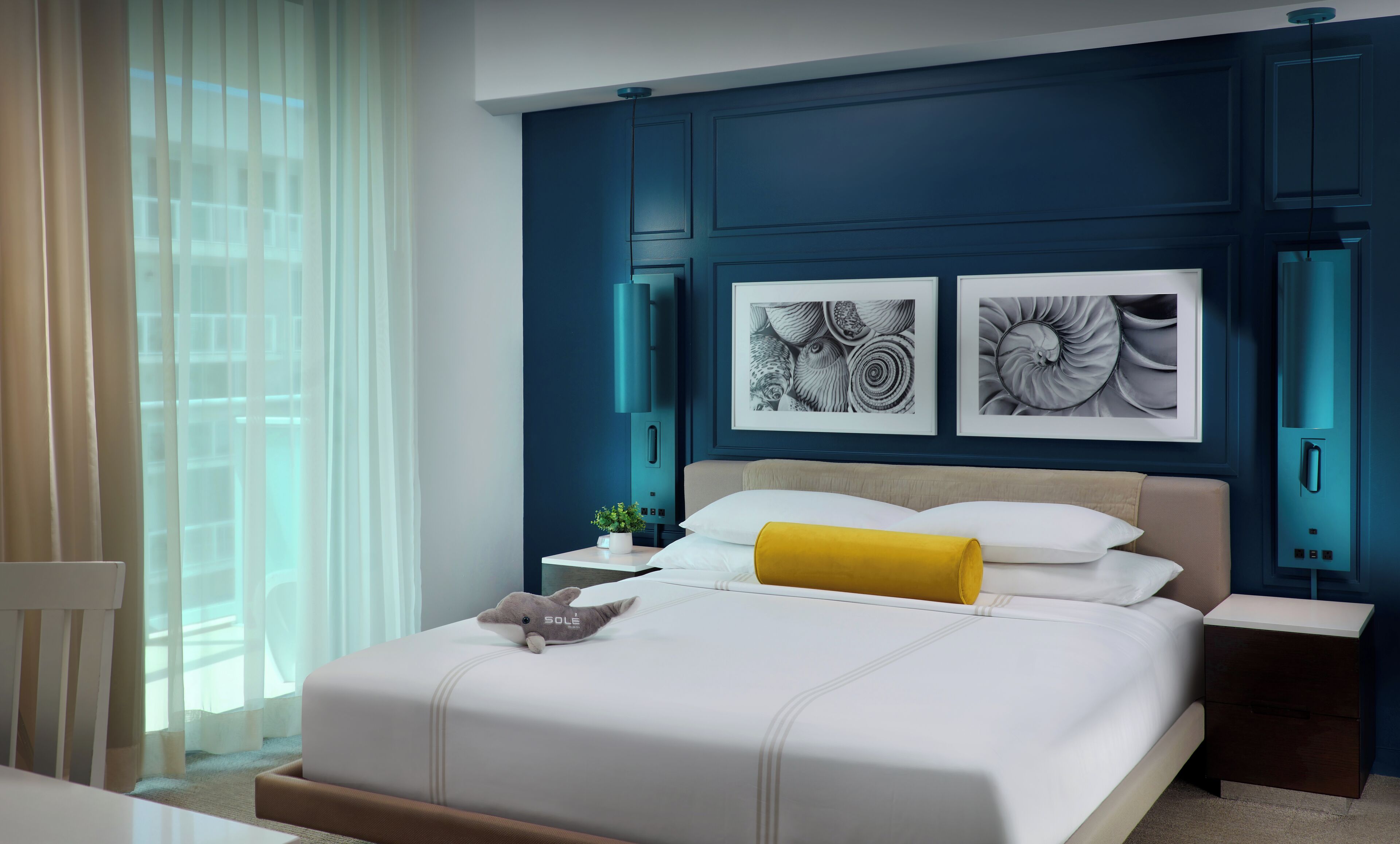A modern hotel room with a large bed, a nightstand, a chair, and artwork on the wall.