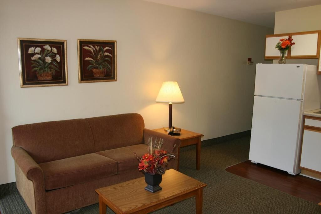 A living room with a brown sofa, a wooden coffee table with a vase, a lamp, and a refrigerator.