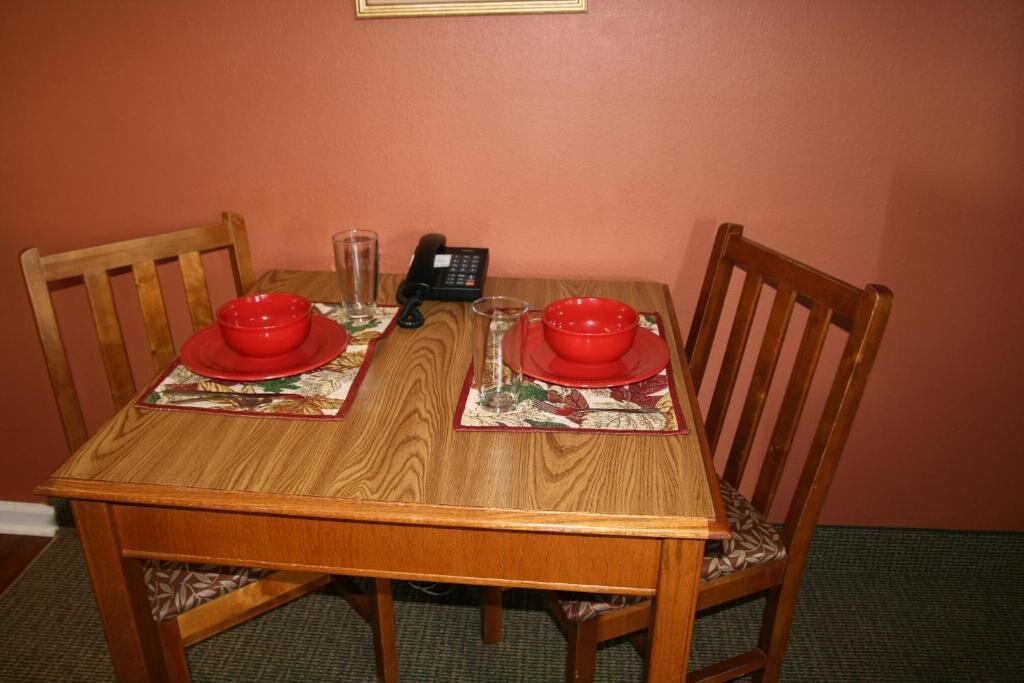 Una mesa de comedor de madera con dos cuencos rojos y un vaso sobre caminos de mesa a juego, un teléfono y un marco de pared.