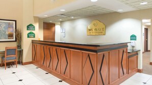 Un comptoir d’accueil avec un revêtement en bois et des motifs géométriques, une œuvre d’art florale encadrée accrochée au mur, et une enseigne indiquant le nom de l’hôtel.