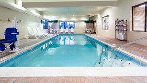 Une piscine intérieure à l’eau claire, entourée de chaises longues blanches et d’un télésiège bleu.