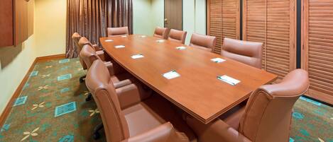 Un salón de conferencias con una larga mesa, sillas de cuero, alfombra estampada y paneles de madera.