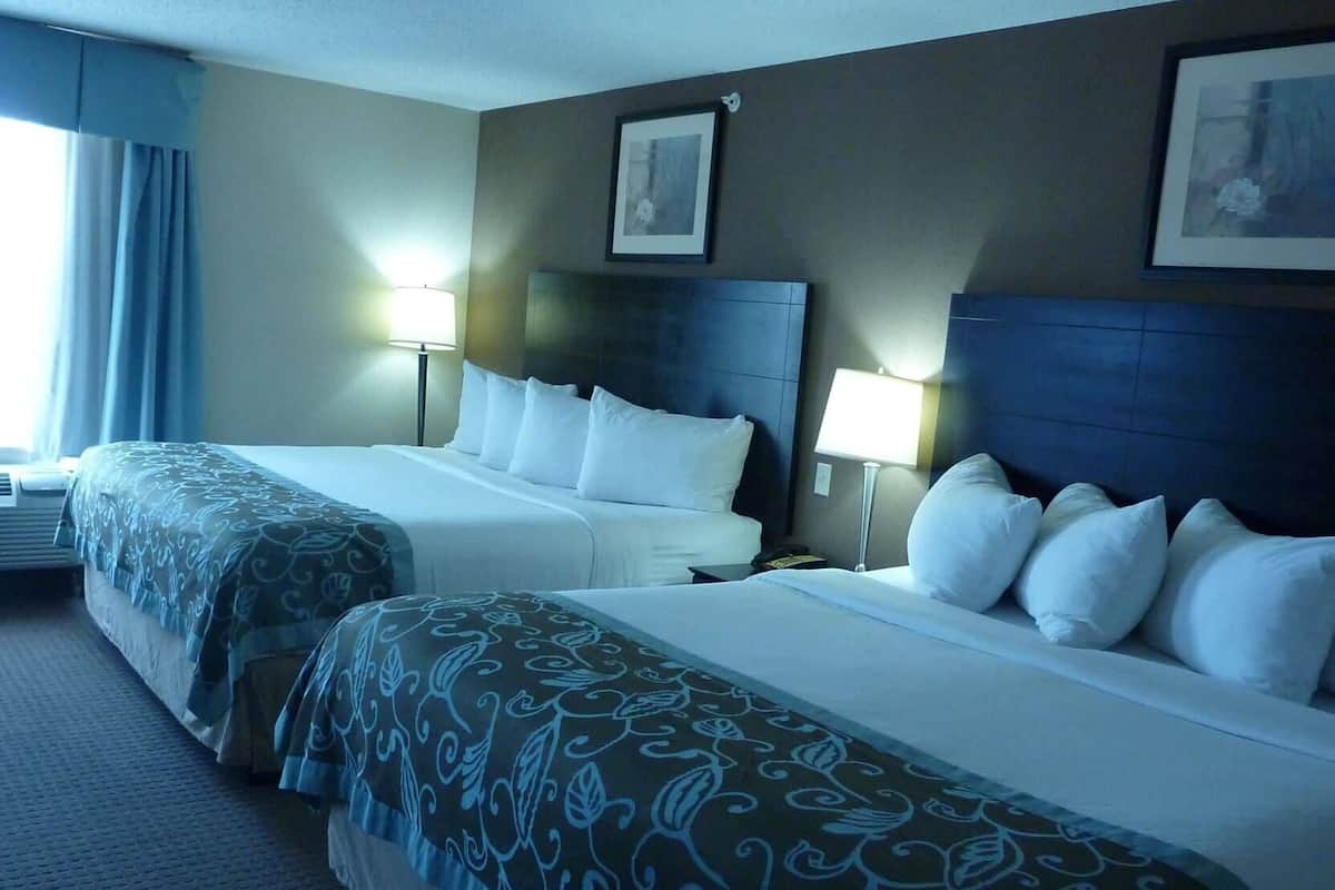 Une chambre d’hôtel avec deux lits, une tête de lit, des lampes de chevet et un tableau encadré au mur.