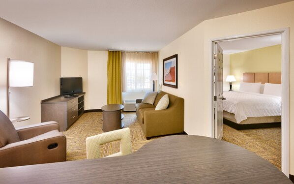 A hotel room with a bed, a TV, a desk, and a sofa. - Candlewood Suites Dallas Plano East Richardson by IHG (Plano)