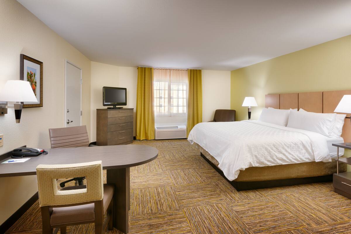 Une chambre d’hôtel équipée d’un lit, d’un bureau, d’une chaise, d’une télévision et d’une fenêtre avec des rideaux.