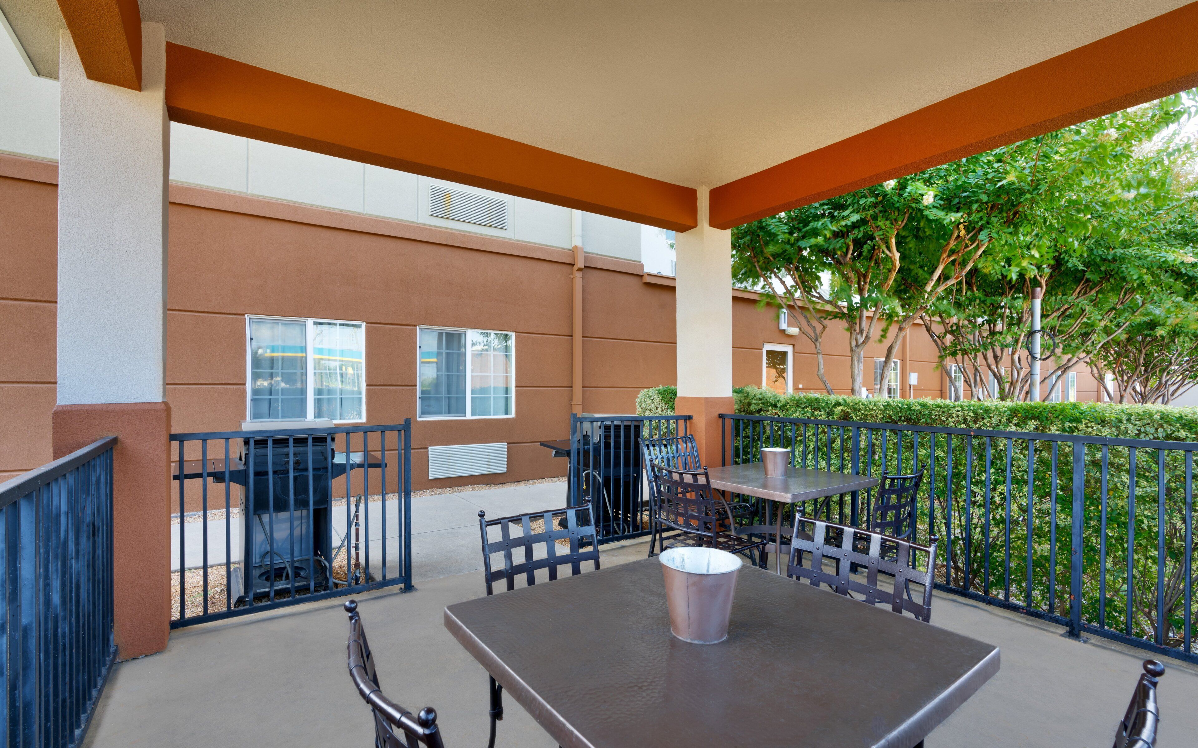 An outdoor patio area with a table and chairs, a trash bin, and a metal fence.