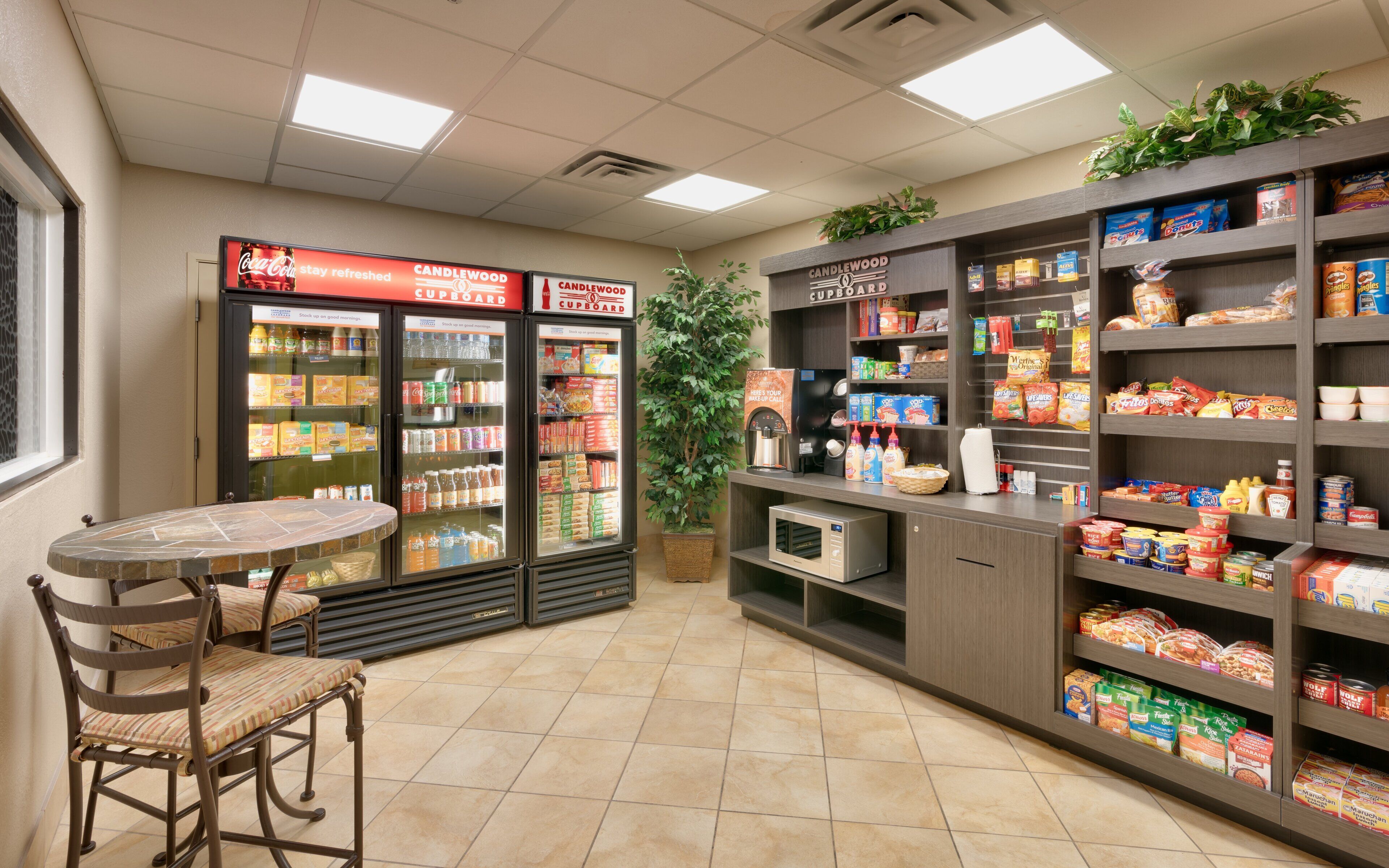 A self-service beverage station with refrigerated drink dispensers and a seating area with a table and chairs.
