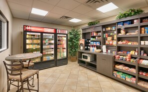 A self-service beverage station with refrigerated drink dispensers and a seating area with a table and chairs. - Candlewood Suites Dallas Plano East Richardson by IHG (Plano)