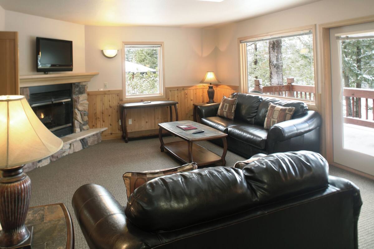 A living room with a fireplace, leather sofa, coffee table, and a TV mounted on the wall.