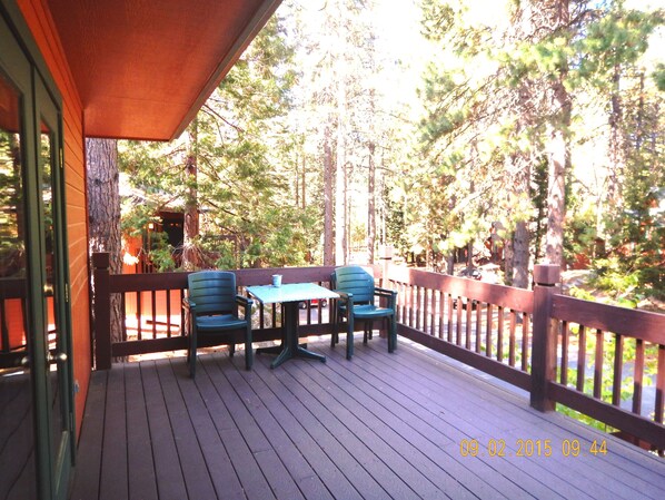 A wooden deck with two chairs and a table, surrounded by a wooden railing and trees.