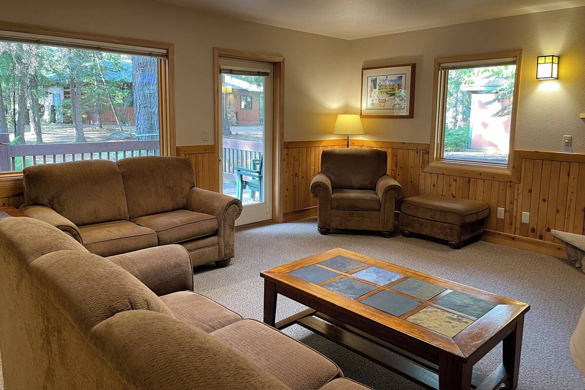 A cozy living room with a sectional sofa, a single armchair, a small ottoman, and a glass-top coffee table.