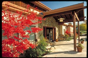 A building with a stone facade, a wooden balcony, and a covered patio area with a bench and potted plants.