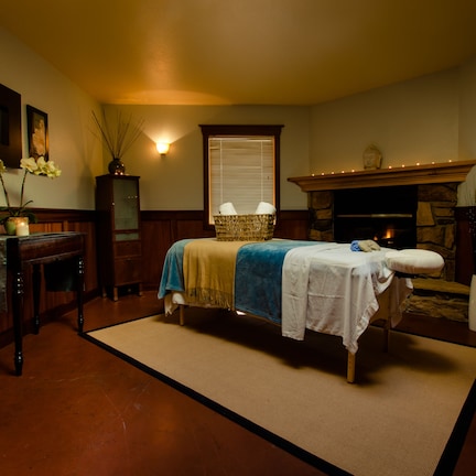 A cozy room with a bed, a wooden desk, a vase with flowers, and a fireplace.