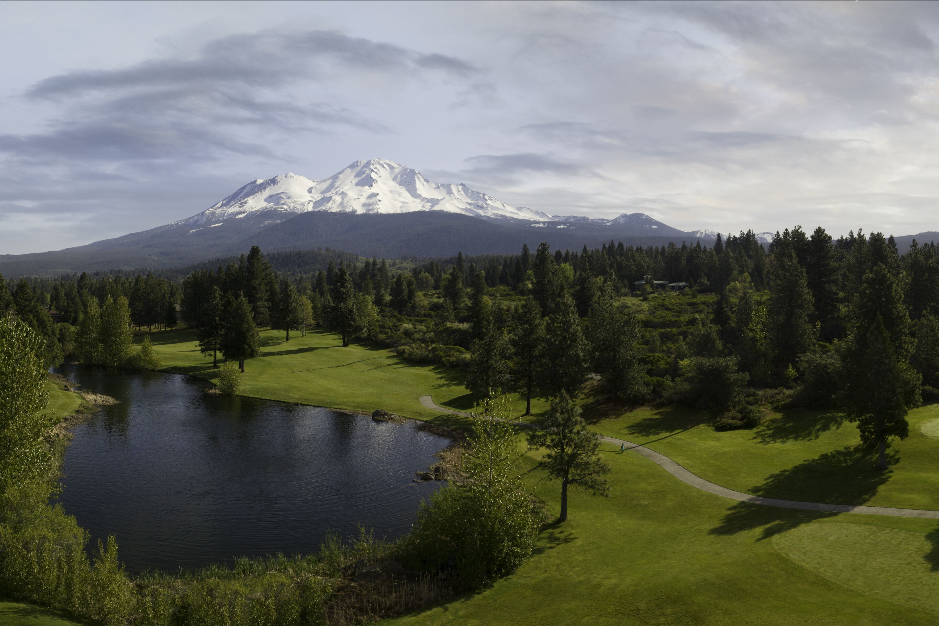 A golf course with a lake, trees, and a mountain in the background.