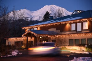 A hotel with a snow-covered mountain in the background, a covered outdoor area, and a car passing by.