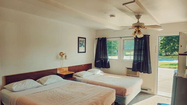 Une chambre d’hôtel avec deux lits, un ventilateur de plafond, une fenêtre avec des rideaux, un tableau encadré au mur et une vue sur l’extérieur.