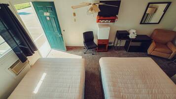 Une chambre d’hôtel avec deux lits, un bureau, une chaise, une télévision, un ventilateur de plafond et une porte.