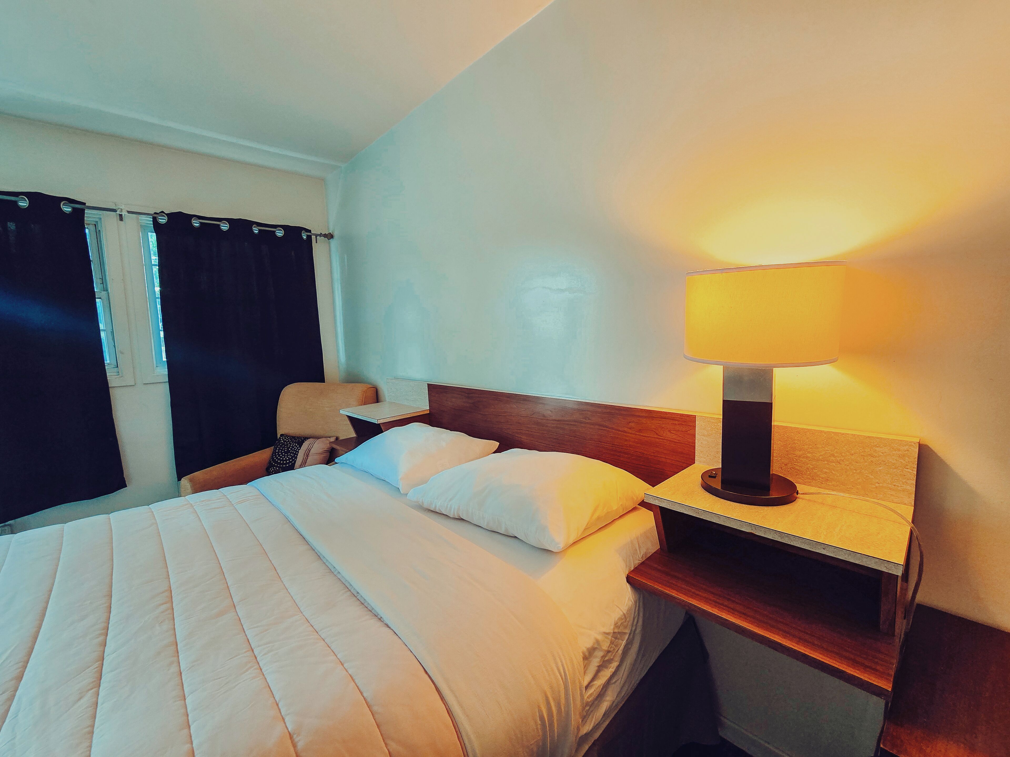 A hotel room with a bed, a nightstand, a lamp, and a window with curtains.