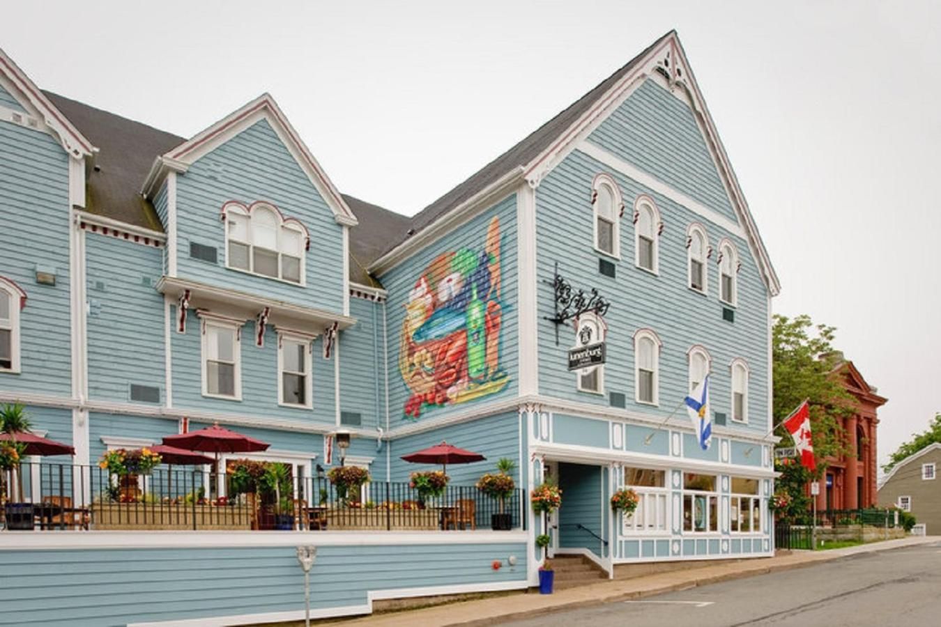 Un bâtiment à deux étages, orné d’une grande fresque sur un de ses murs, avec une devanture de magasin portant une enseigne et un drapeau canadien.